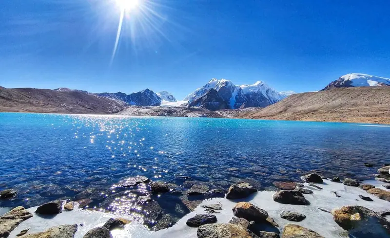 A glacial lake beneath snow peaks, sparkling in high-altitude sun