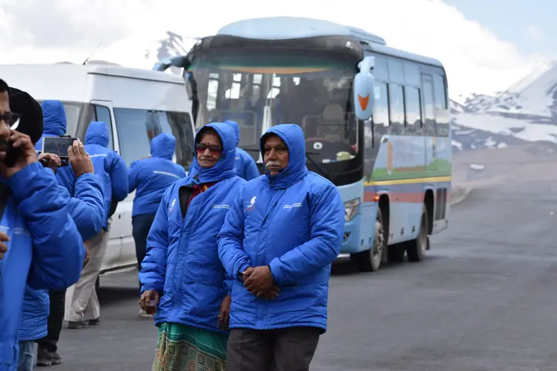 Yatris in matching blue jackets beside the tour coaches on the Tibetan plateau