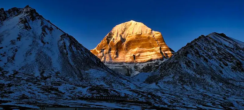 Mount Kailash lit gold at dusk above dark ridges
