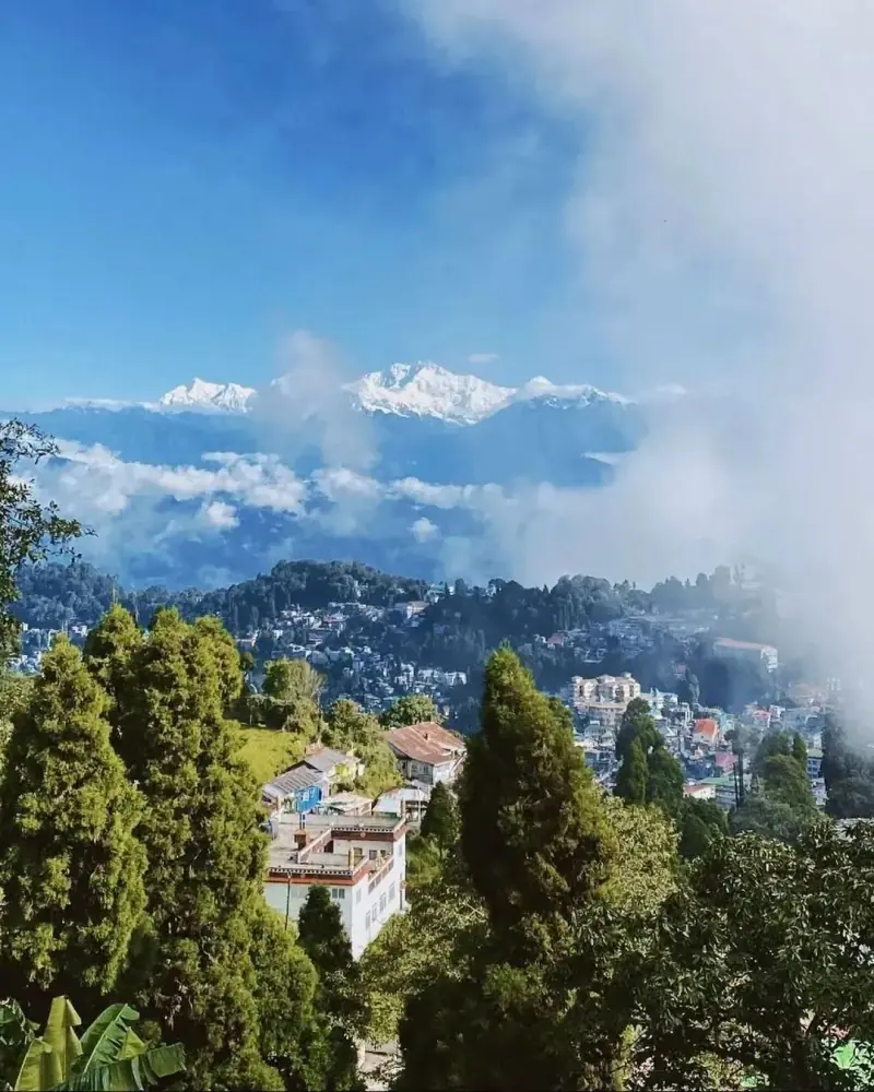 A hill town under drifting cloud, with snow peaks on the horizon