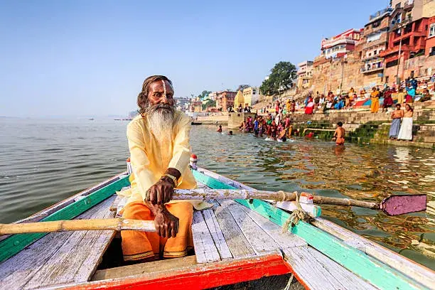 A sadhu seated in a boat on the Ganga, ghats behind